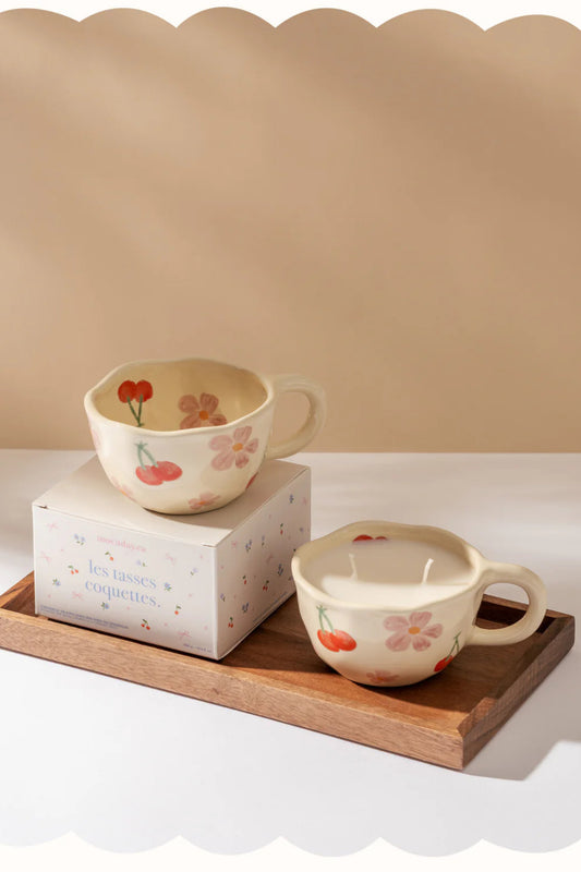 Bougies parfumées en tasses céramique crème avec motifs fleurs et cerises présentées sur un plateau décoratif.