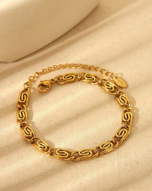 Bracelet en acier inoxydable plaqué or 18k avec maille trombone stylisée sur fond beige texturé