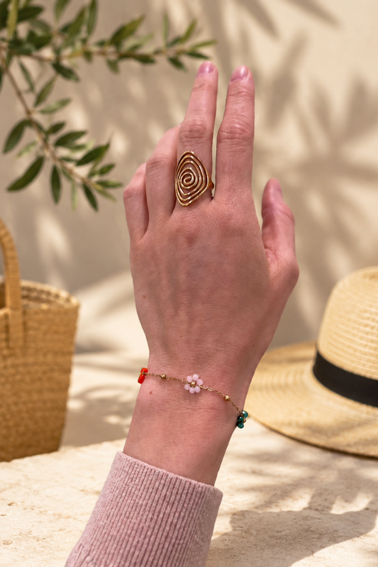 Bracelet doré fleuri multicolore porté au poignet dans un décor estival bohème