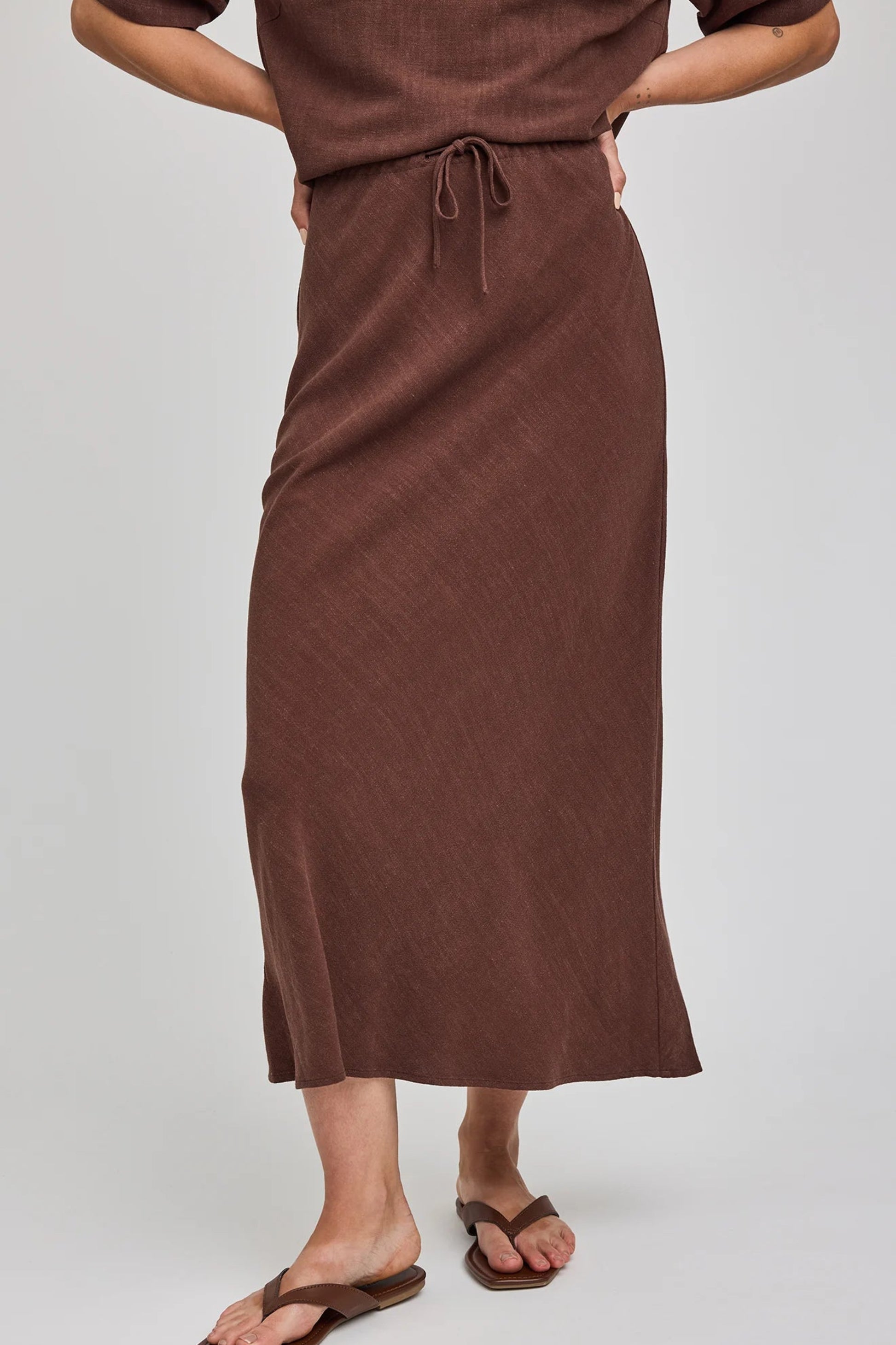 Jupe midi Britanny espresso portée de face avec taille ajustable, cordon et tombé fluide en rayonne et lin.
