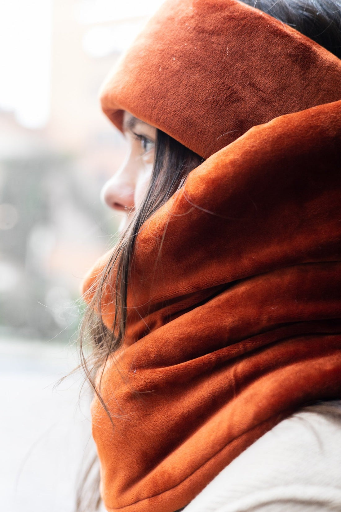 Cache cou très large, épais et doux de couleur orange foncé. Se passe directement par-dessus la tête. Le modèle porte un bandeau assorti et un manteau beige. 