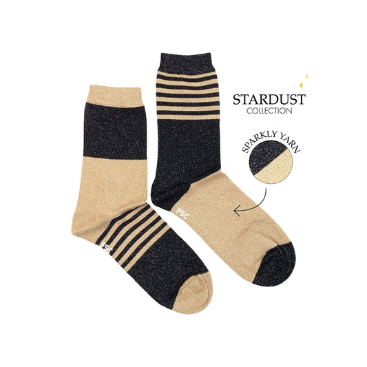 Paire de chaussettes dépareillées sur fond blanc. Les deux chaussettes sont de couleur or et noir et les motifs s’alternent entre des lignes et des larges bandes. Ce sont des chaussettes à paillettes.  