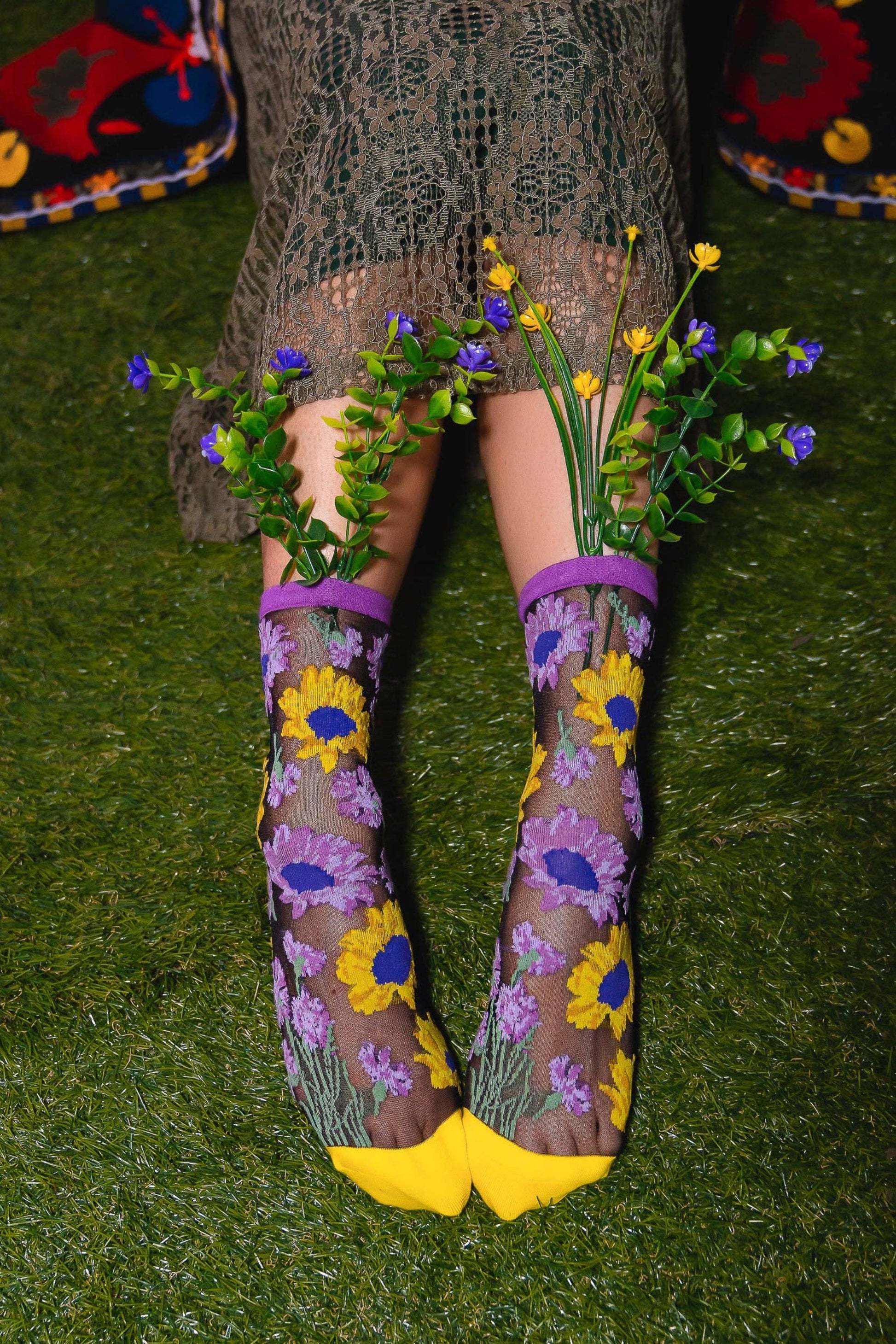 Chaussettes transparentes noires à fleurs violettes et tournesols jaunes portées sur gazon