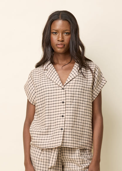 Chemise fluide beige avec un imprimé à carreaux noirs. Ce haut à manches courtes présente une coupe ample et confortable, idéale pour un look décontracté et élégant. Il est doté d’un col à revers ouvert et d’une patte de boutonnage sur le devant, apportant une touche classique et intemporelle. Confectionnée dans une matière légère et respirante, cette chemise est parfaite pour la saison estivale. 