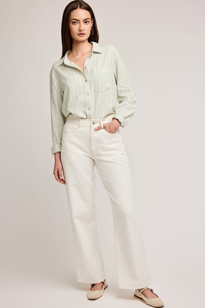 Chemise rayée vert sauge portée de face avec coupe fluide et boutons, portée avec un jeans blanc