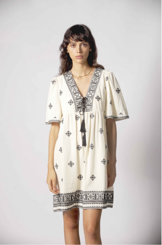 Détail de la robe Clelia blanc avec encolure en V brodée, cordons à pampilles et motifs noirs.