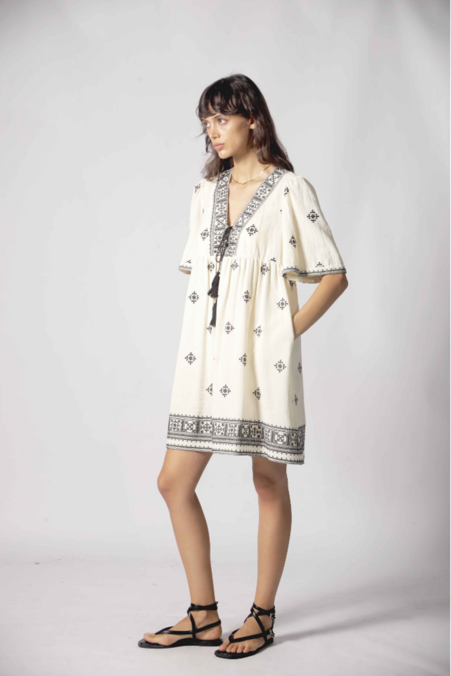 Robe courte Clelia blanc portée de côté avec encolure brodée, cordons à pampilles et style bohème chic.