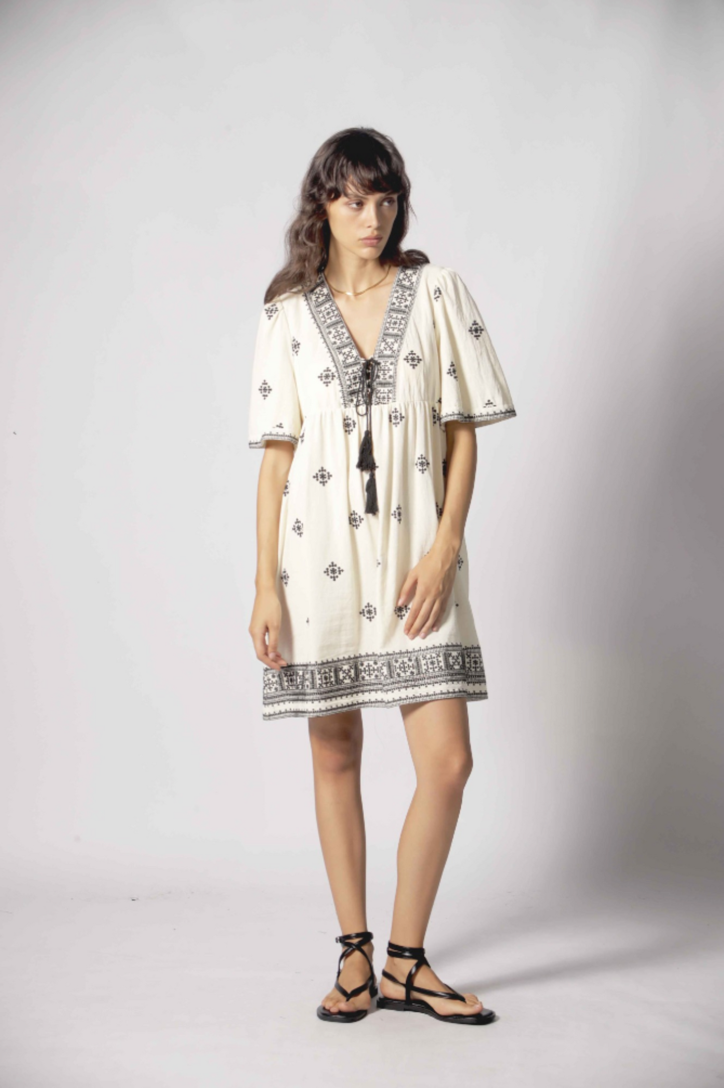 Robe courte Clelia blanc portée de face avec broderies noires, manches amples et coupe légère en coton.