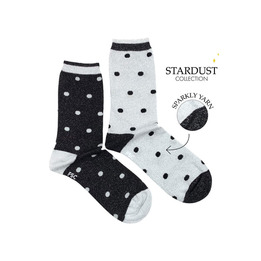 Paire de chaussettes dépareillées sur fond blanc. Une chaussette a des pois gris clairs sur un fond noir et l’autre des pois noirs sur un fond gris clair. Ce sont des chaussettes à paillettes.  