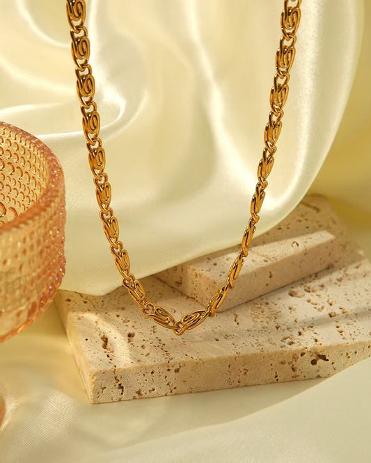 Collier en acier inoxydable plaqué or 18k à maille tressée stylisée sur fond crème luxueux