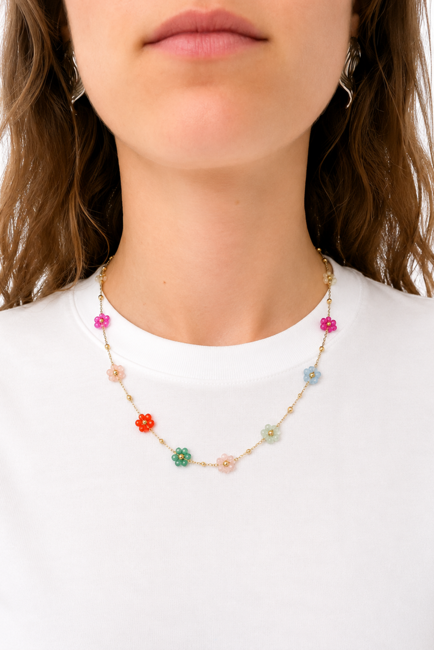 Collier doré avec petites fleurs pastel colorées porté sur un chandail blanc minimaliste