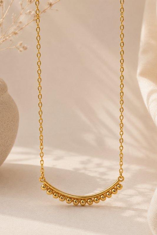 Collier minimaliste doré en or vermeil avec rangée de billes sur chaîne fine élégante dans un décor beige lumineux