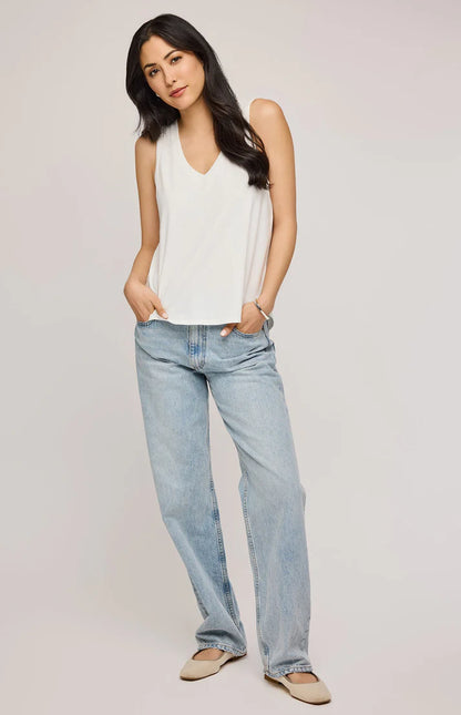 Débardeur Gisele blanc à encolure en V. Ce haut sans manches présente une coupe fluide et légère, idéale pour un confort optimal au quotidien. Son design minimaliste s'adapte facilement à différents styles, que ce soit pour un look décontracté avec un jean clair ou pour une tenue plus habillée sous une veste. Le mannequin porte le débardeur avec un jean droit délavé et des ballerines beiges, créant une allure simple et élégante.
