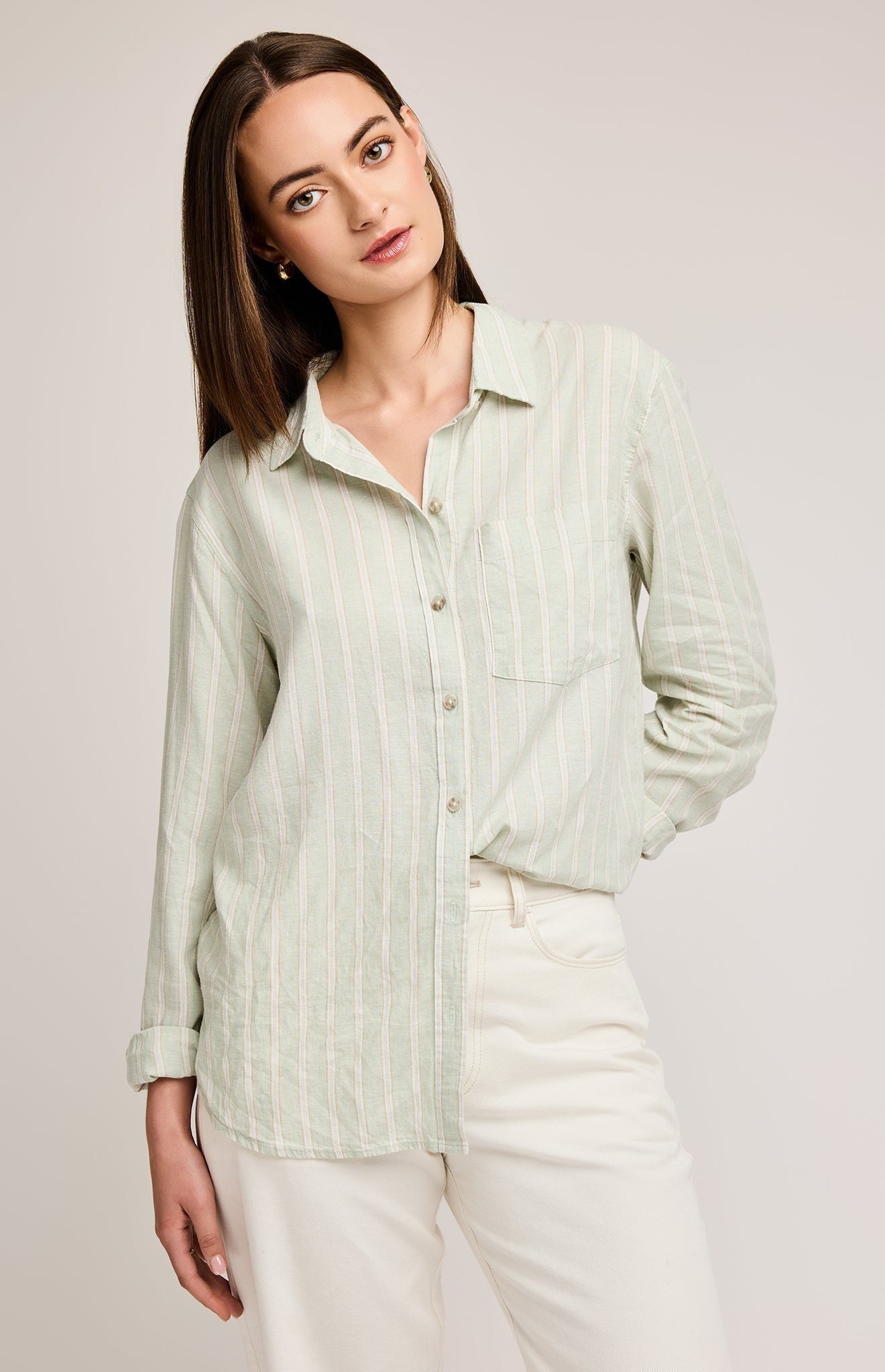 Chemise boutonnée de couleur vert pastel avec des rayures blanches et marron. Le model porte un pantalon plan, un pan de la chemise est rentré dans le pantalon. L'arrière-plan est un fond gris.