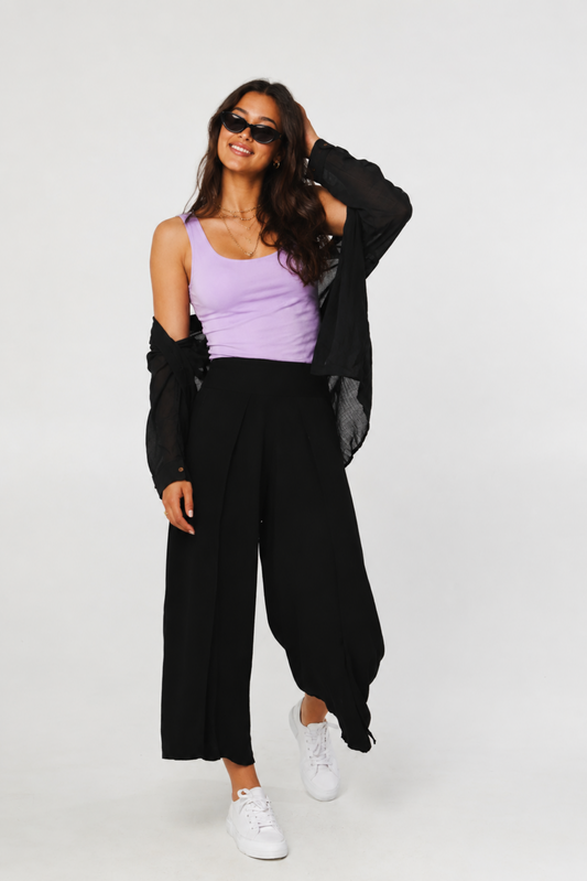 Femme portant le pantalon Dubai noir avec une camisole mauve, une chemise noire légère et des baskets blanches, avec coupe fluide et taille élastique.
