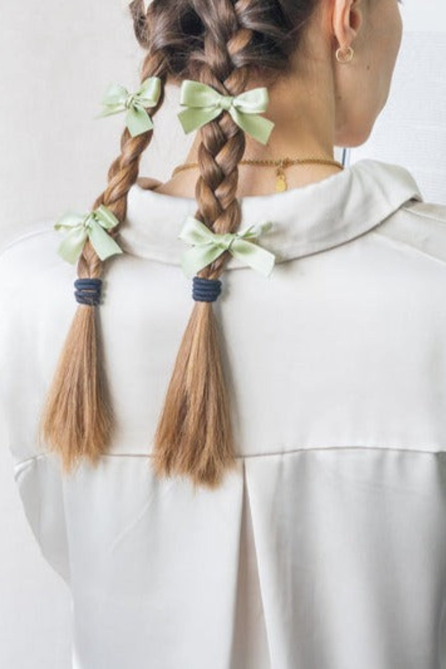 Femme portant deux mini boucles en satin vert sauge dans ses tresses, vue arrière sur les cheveux.