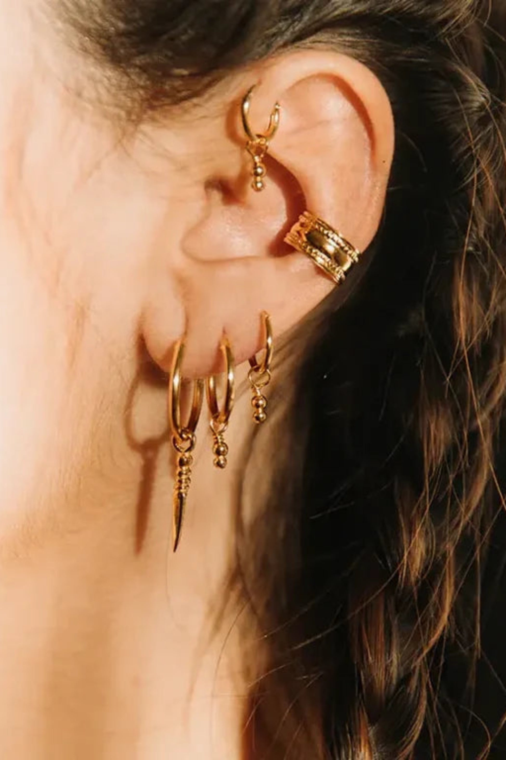 Ear cuff Aya I porté sur l’oreille avec plusieurs boucles d’oreilles dorées en accumulation.
