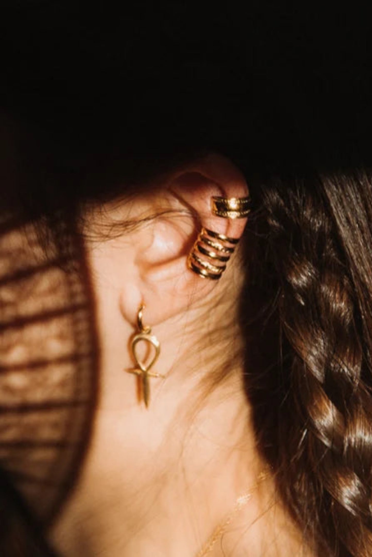 Ear cuff Aya III porté sur le cartilage de l’oreille avec d’autres bijoux dorés.