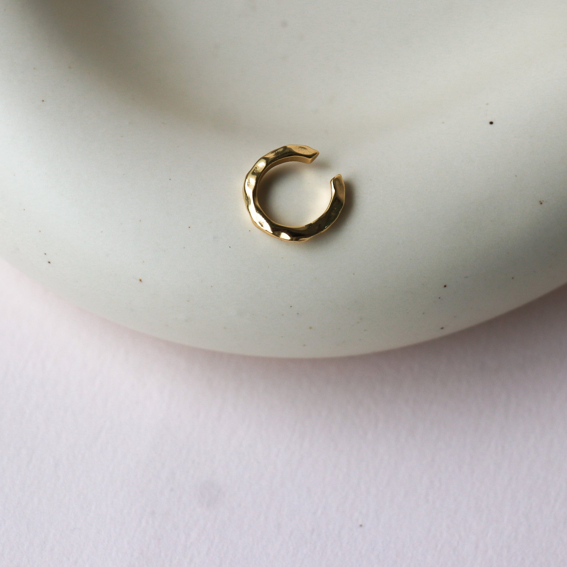 Petite bague d'oreilles dorée martelé présentée sur une assiette en porcelaine. C'est un plan rapproché. L'arrière-plan est un fond rose.