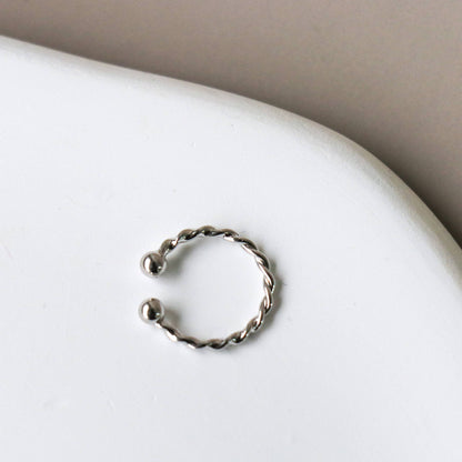 Ear cuff torsadé argent vu de face sur fond marbré - Finition argentée brillante