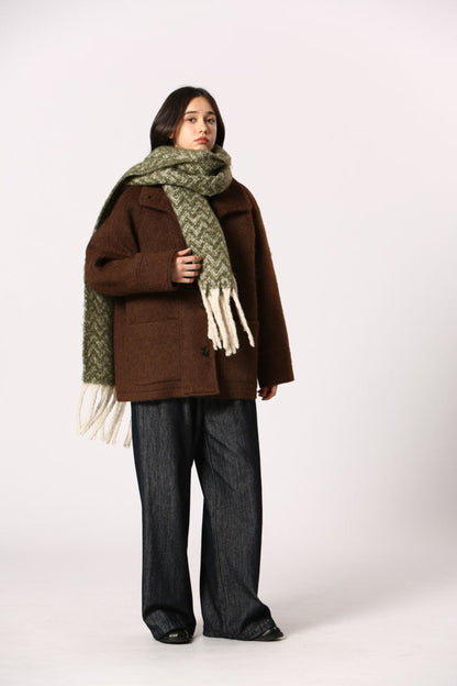 Écharpe verte à motif chevron avec franges blanches, portée sur manteau brun
