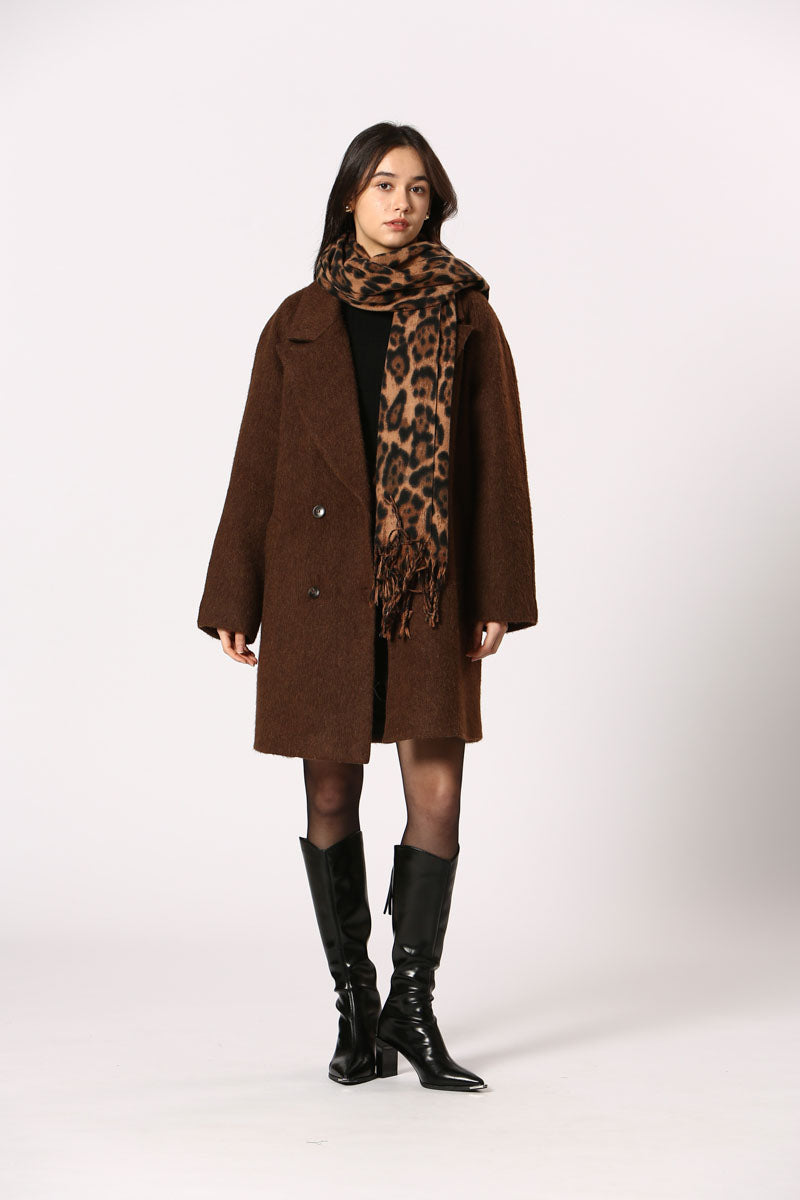 Femme debout avec l’écharpe Kylie brun léopard, tenue chic avec manteau et bottes hautes