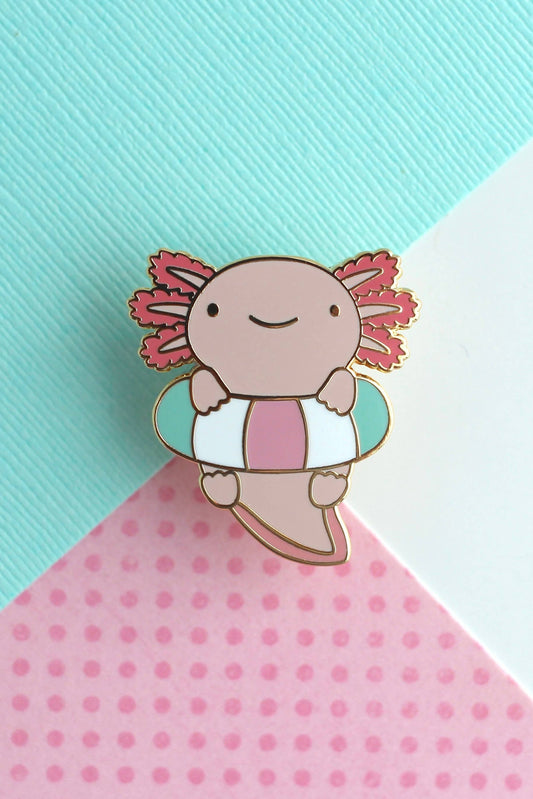 Gros plan sur l’épingle Axolotl Flottant – métal doré, émail rose et bleu pastel.