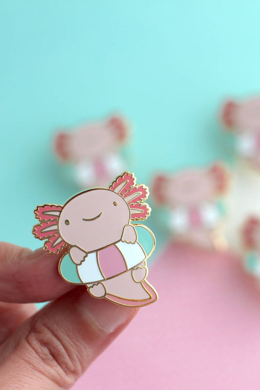Épingle Axolotl tenue entre les doigts, mettant en valeur les détails dorés et la bouée pastel.