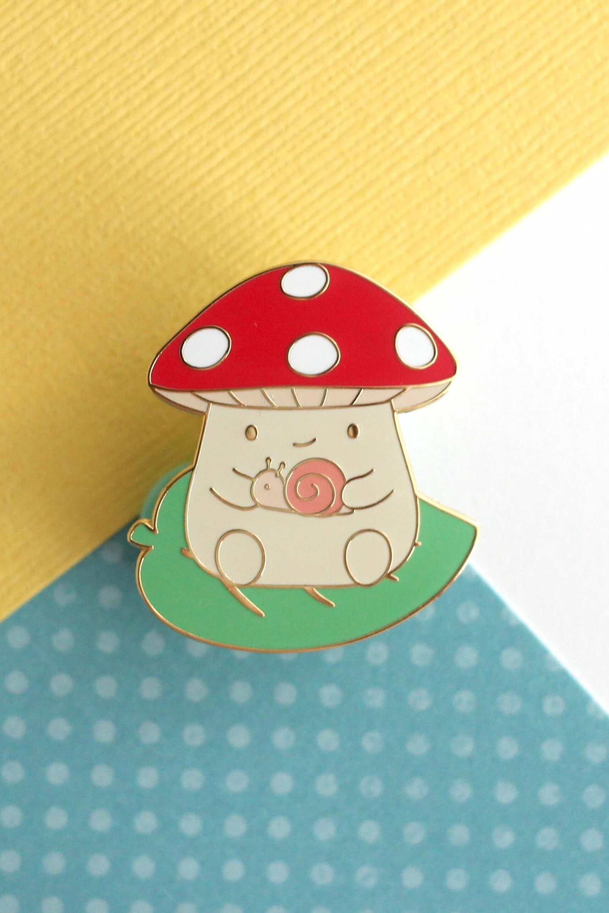 Épinglette champignon rouge avec escargot en émail dur posée sur fond coloré