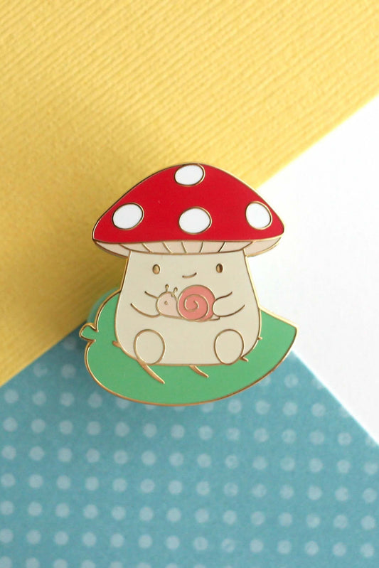 Épinglette champignon rouge avec escargot en émail dur posée sur fond coloré