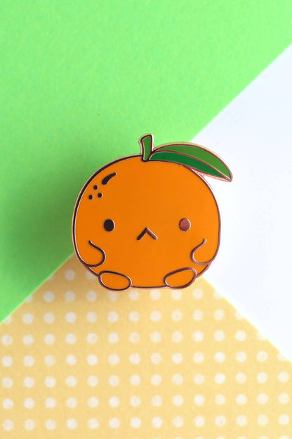  Épinglette en forme de clémentine vue de face sur fond vert et jaune à pois.