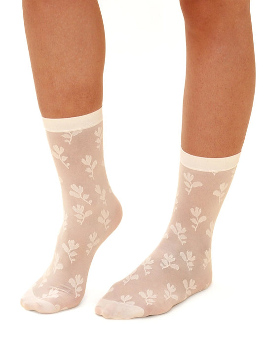 Chaussettes transparentes qui monte au-dessus de la cheville. Elles sont de couleur crème avec un motif floral. On voit quelqu'un porter la paire de chaussettes sur un fond blanc.