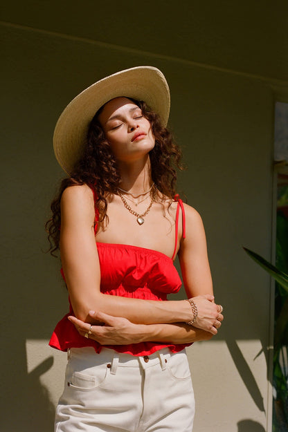 Femme au soleil avec le haut rouge et un chapeau, yeux fermés et bras croisés