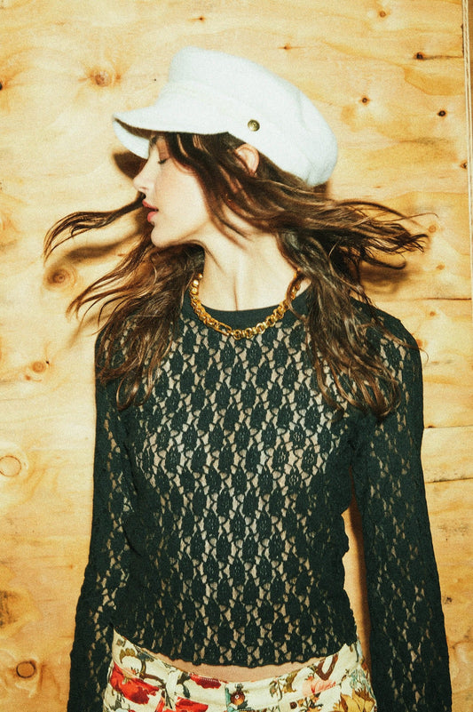 Haut Mathilda en dentelle noire porté avec chaîne dorée, chapeau blanc et pantalon à fleurs