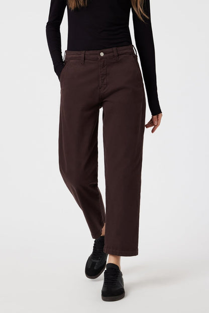 Pantalon de type chino à jambes droites en coton de couleur violet très foncé qui tend vers le marron. Le modèle le porte avec un col roulé noir et des chaussures fermées noires.