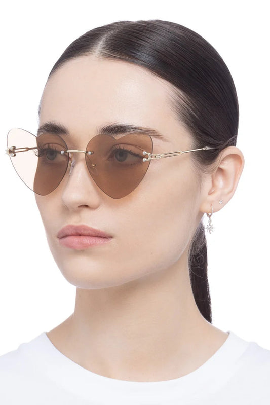 Lunettes de soleil Lucie Marbre Or portées par un mannequin, avec verres beige en forme de cœur et monture dorée fine.