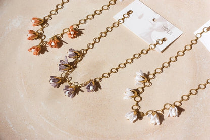 Trois colliers Malli posés à plat – fleurs en textile corail, lavande et blanc sur chaîne dorée