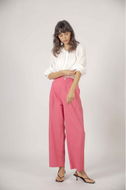 Pantalon droit rose vif porté avec sandales minimalistes et blouse blanche