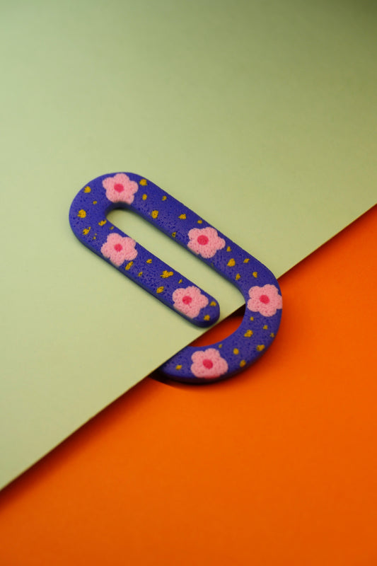 Marque-page en argile polymère bleu glissé sur une feuille – motif fleuri