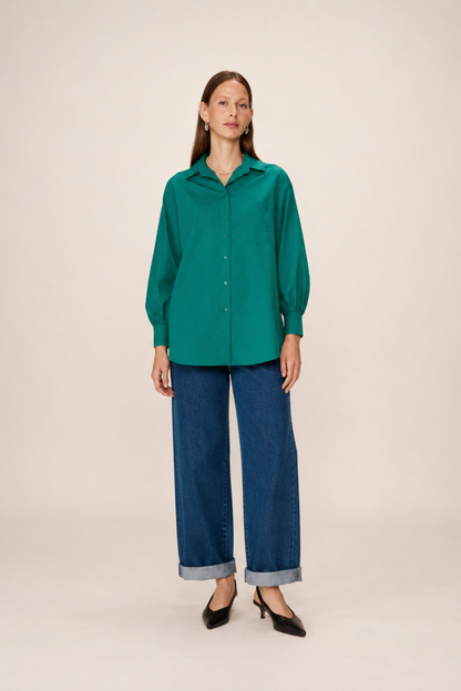Chemise longue verte portée de face avec col classique, poche poitrine et coupe oversize.