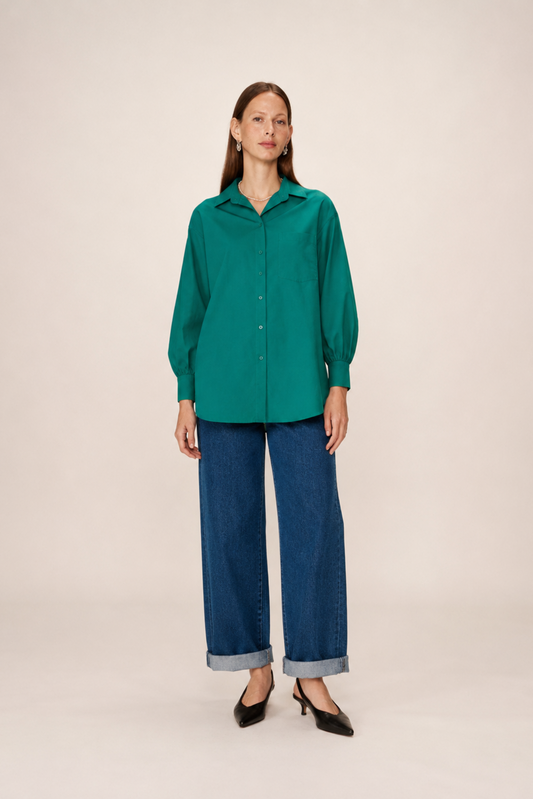 Chemise longue verte portée de face avec col classique, poche poitrine et coupe oversize.