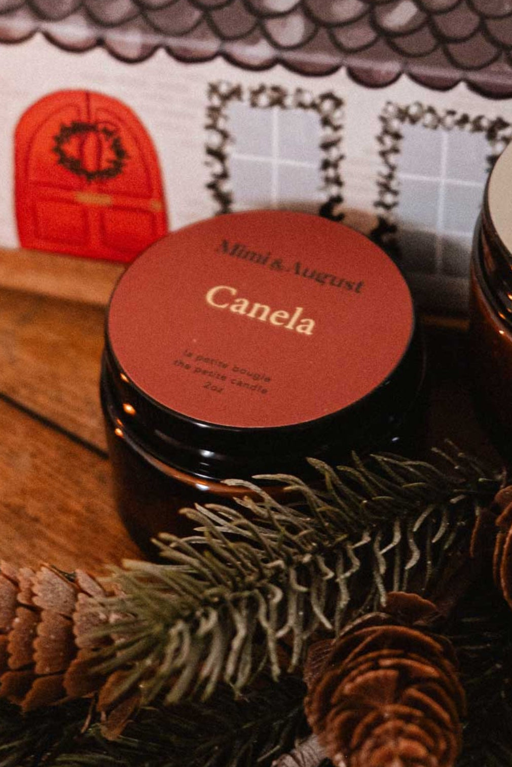 Mini bougie Canela sur table décorée de branches de pin, ambiance chaleureuse parfum epice