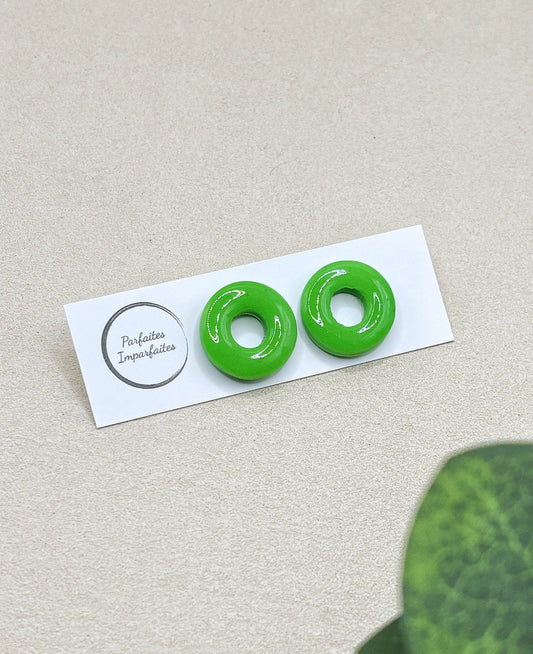 Petites boucles d'oreilles ronde avec un trou au centre. Elles sont vernis ce qui leur donne vraiment l'apparence de bonbons. Elles sont entièrement vertes pomme. Les boucles d'oreilles sont présentées sur un carton blanc avec le logo de la marque Parfaites Imparfaites et l'arrière-plan est un fond beige. 