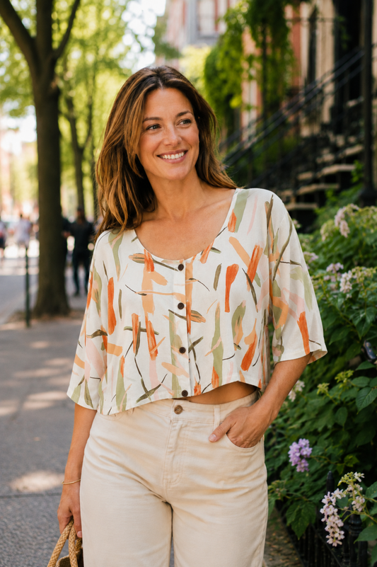 Blouse Nao Orange portée avec pantalon clair, imprimé abstrait orangé et boutons sur le devant.