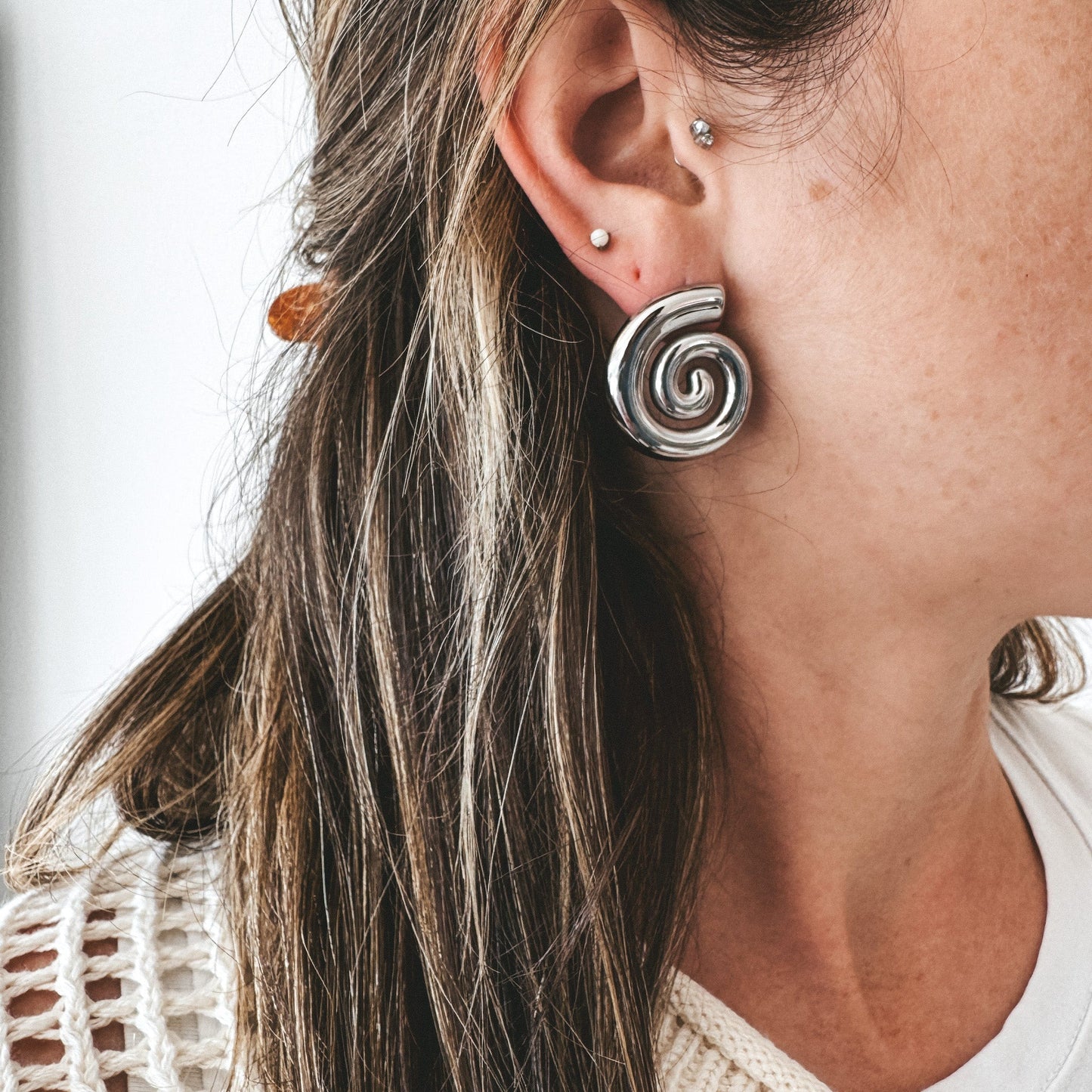 Boucles d'oreilles argent en acier inoxydable en forme de spirale. Le modèle porte aussi un clous d'oreille, de la même marque, avec une pierre blanche. 