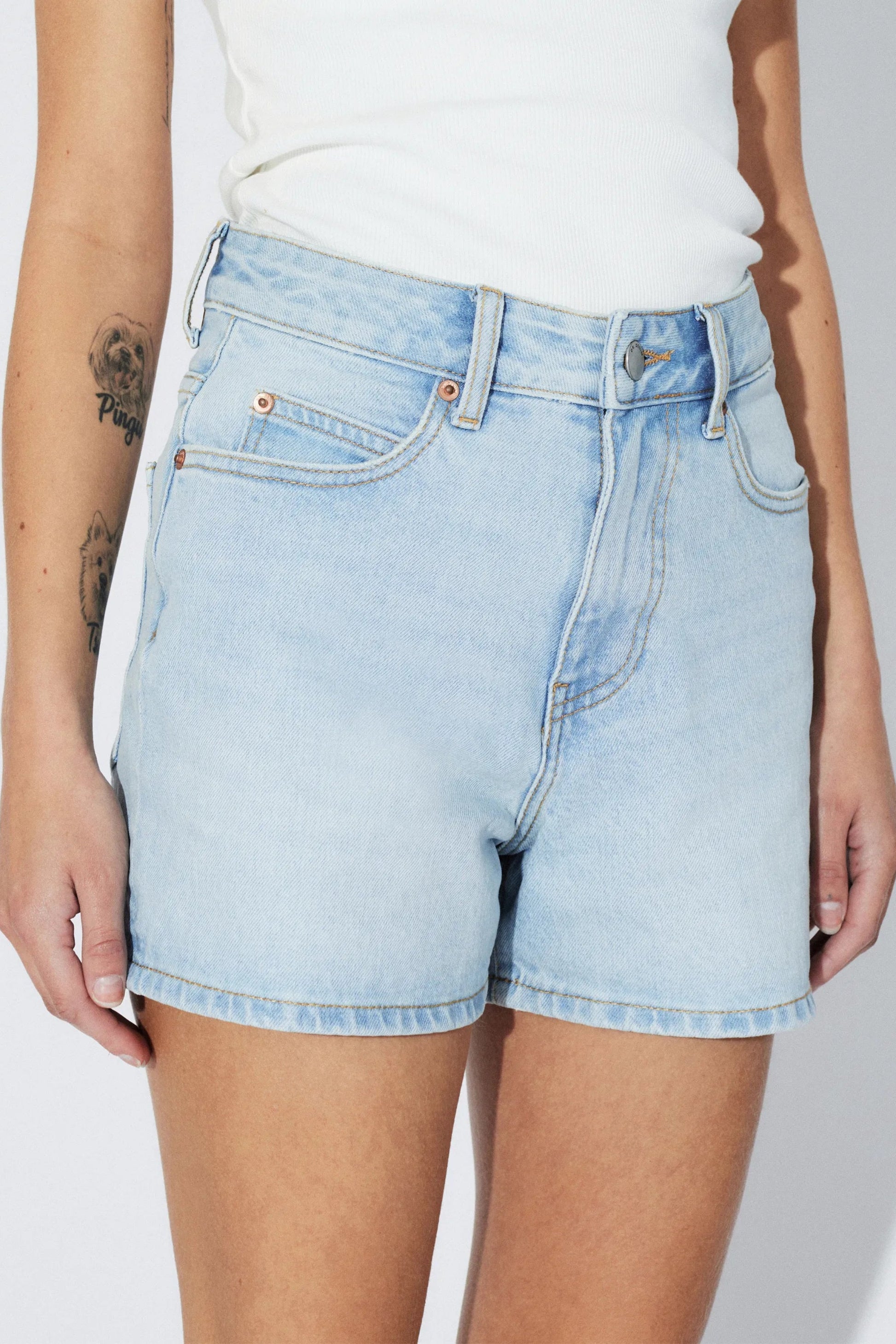 Détail devant du short Nora bleu denim clair avec poches classiques, bouton et braguette zippée.