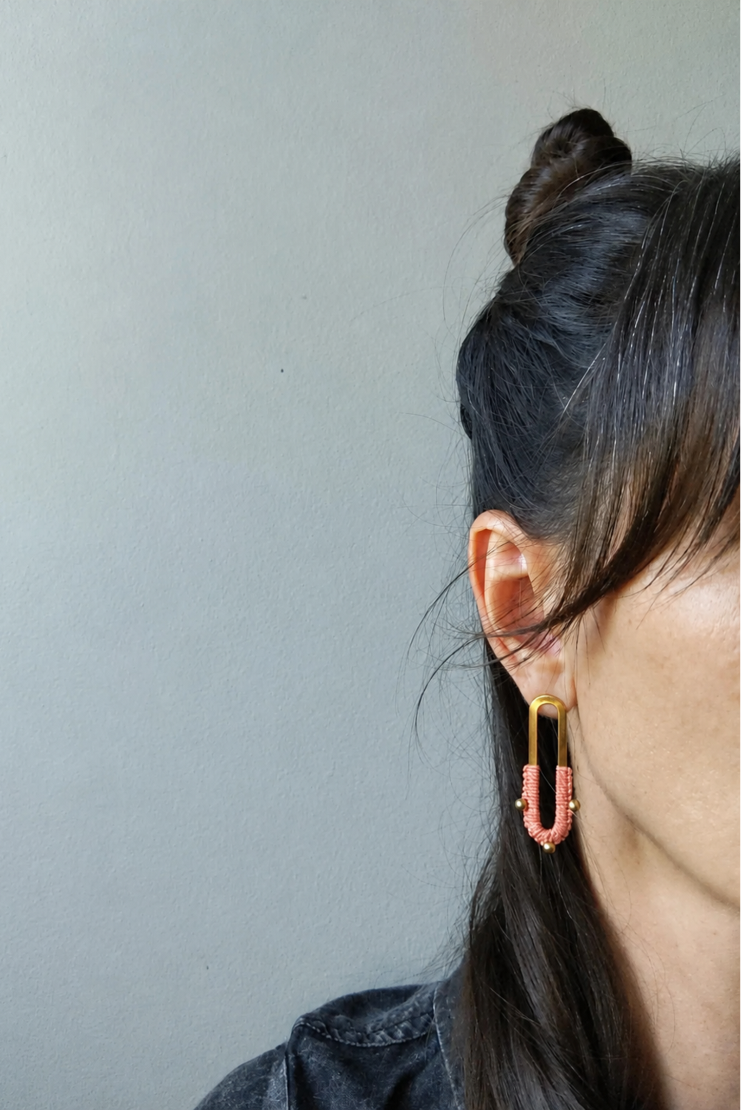 Boucles d’oreilles Nyx Corail portées à l’oreille, bijou long en laiton avec détail de micro macramé.