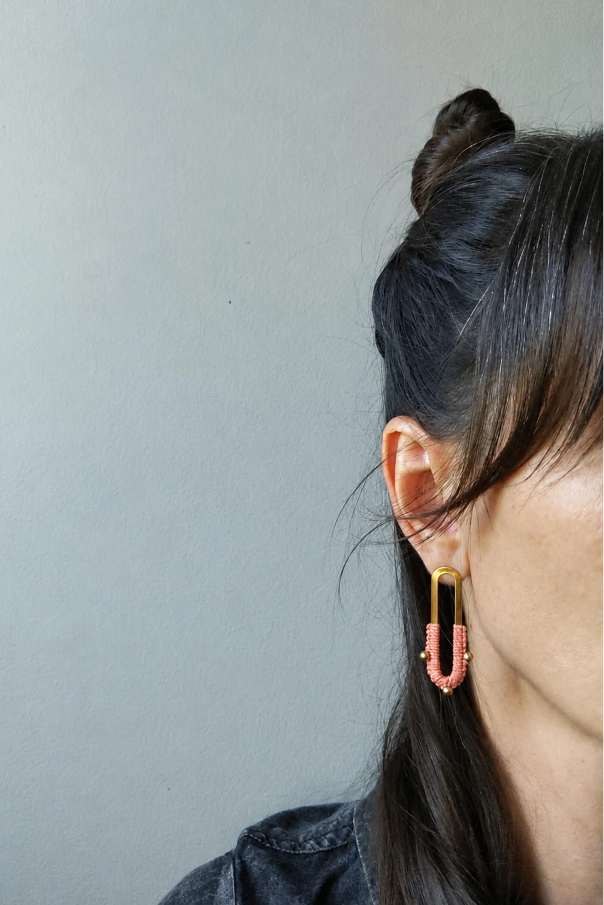 Boucles d’oreilles Nyx Corail portées à l’oreille, bijou long en laiton avec détail de micro macramé.