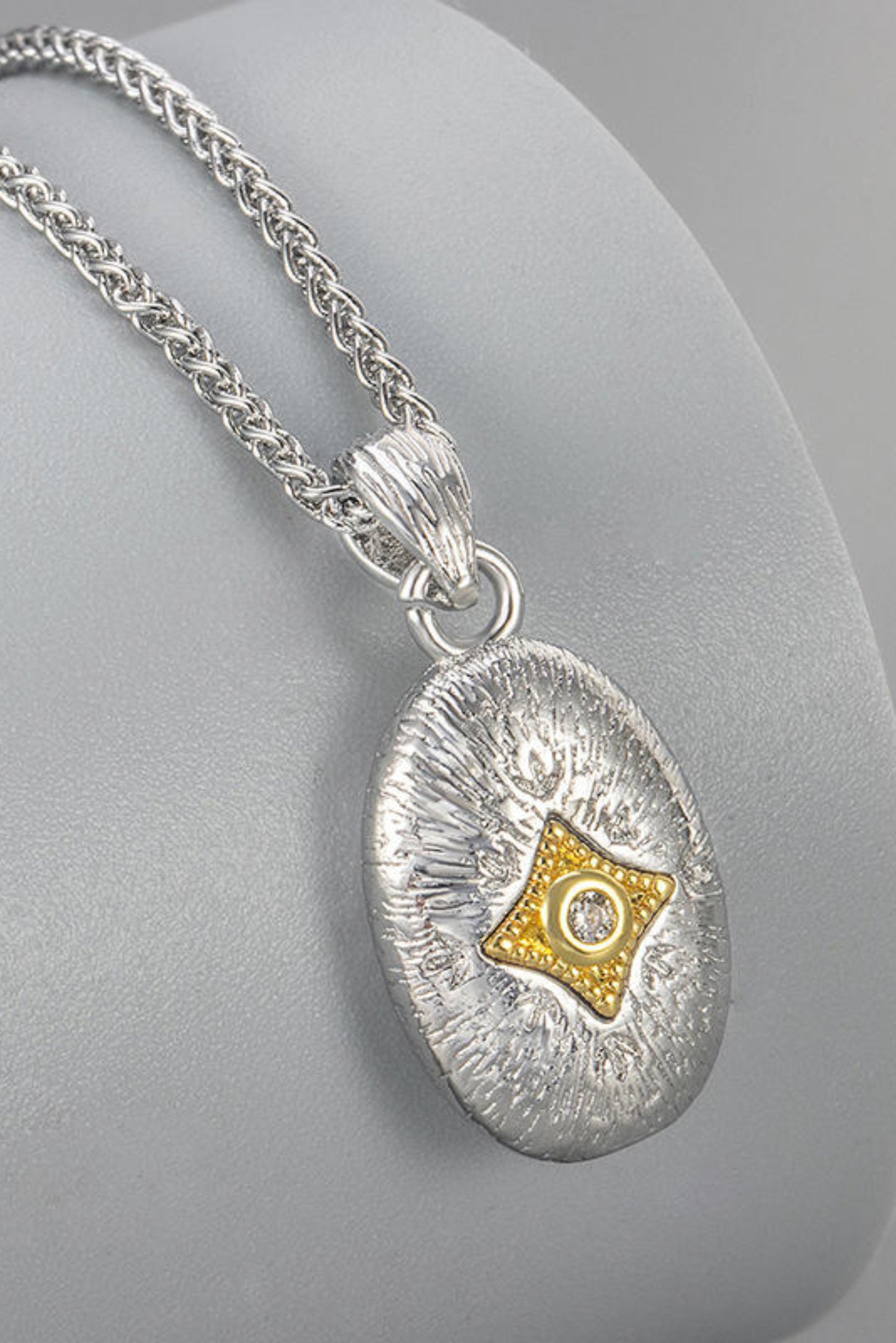 Collier Opale argenté avec médaille ovale texturée, détail doré et pierre brillante au centre.