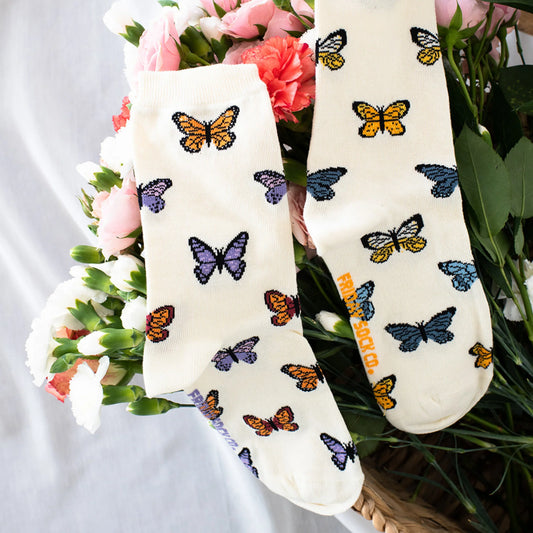 Chaussettes papillons écrues posées sur un lit de fleurs, motif coloré